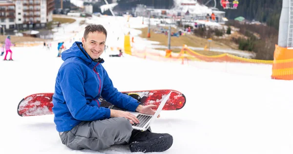 Молодий сноубордист використовує ноутбук на засніженій горі. Білий сніг і блакитне небо. Копіювати простір для реклами . — стокове фото