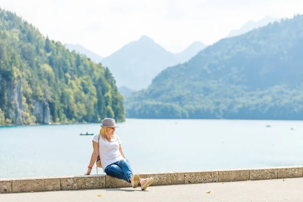 Schöne Touristin mit Hut und Rucksack, die einen atemberaubenden Blick auf die bayerischen Berge in der Nähe von Schloss Neuschwanstein genießt. Reisekonzept. Naturbetrachtung — Stockfoto