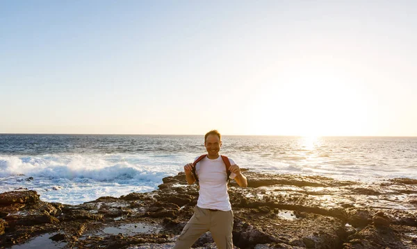 Ein junger Mann auf den Felsen und blickt auf den Ozean, während vor ihm eine große Welle bricht — Stockfoto