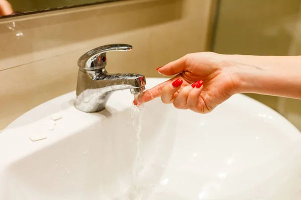 Frau, die ein Bad zu Hause nimmt und die Temperatur überprüft, die fließendes Wasser mit der Hand berührt. Nahaufnahme an Fingern unter heißem Wasser aus dem Wasserhahn eines Waschbeckens oder einer Badewanne im Badezimmer des Hauses. — Stockfoto
