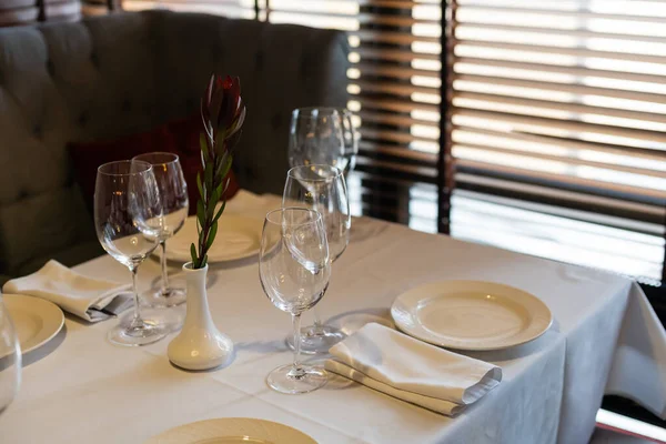 Tableware Glasses, flower fork, knife served for dinner in restaurant with cozy interior. Stock Photo