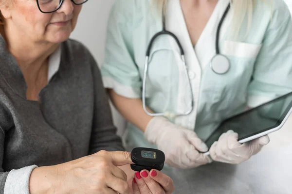 Arzt spricht mit alter Patientin über Krankheitssymptome, Arzt benutzt Fingerkuppen-Pulsoximeter mit alter Patientin, Gesundheits-Check für Senioren und Gesundheits-Screening, Medizintechnik — Stockfoto