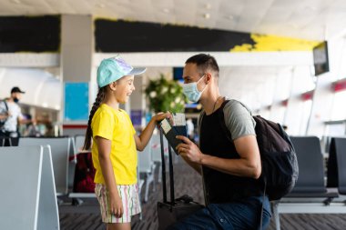 Baba ve kızı koruyucu tıbbi maskeler takıyor. Havaalanında ya da alışveriş merkezinde dezenfektan kullanıyorlar. Virüs ve hastalık koruması