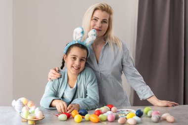 Tavşan kulaklığı takan neşeli aile modern aydınlık mutfakta toplanıyor ve Paskalya yumurtalarını birlikte acıtıyorlar..