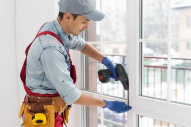 Tamirci, beyaz plastik pencereyi içeri ayarlıyor. İşçi, pencereyi onarmak için tornavida kullanıyor. ev ödevi.