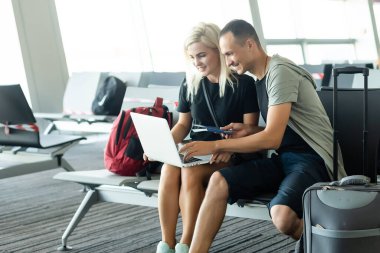 Havaalanındaki bekleme salonunda dizüstü bilgisayarı, telefonu ve bavulu olan çift oturuyor. İş seyahati kavramı