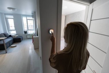 Akıllı ev sistemini kullanan ya da evden çıkmadan önce modern alarm sistemini çalıştıran hoş bir kadın. Mutlu kadın eve ya da daireye döndüğünde kolay güvenlik teknolojisini kapatıyor..