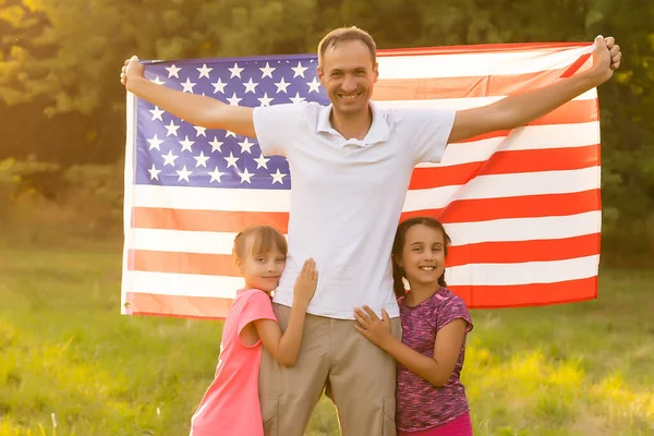 Familia feliz en el campo con EE.UU., bandera americana en la espalda. Imágenes de stock libres de derechos