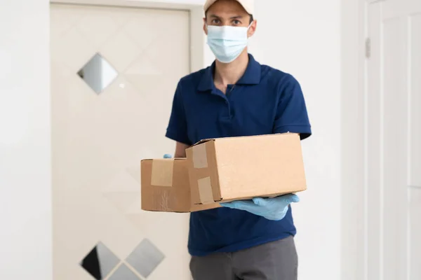 Μεταφορέας με προστατευτική μάσκα και γάντια που κρατάει κουτί με ψώνια μπροστά από μια πόρτα — Φωτογραφία Αρχείου