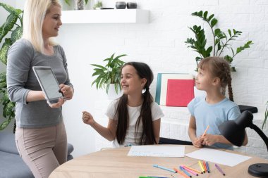 Anne ve iki kız evde ödev yapıyor ve kitap okuyor.