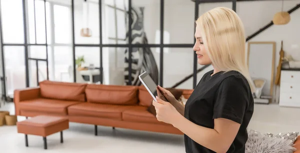 Vrouw gebruik toepassing voor smart home control op tablet. Interieur van woonkamer op de achtergrond. — Stockfoto