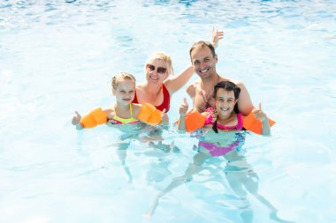 Denizde tropik bir tatil köyünde mavi yüzme havuzunda oynayan mutlu bir aile. Yaz tatilleri konsepti.