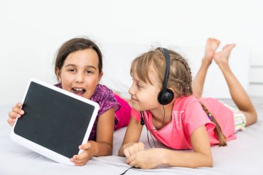 ev, eğlence, yeni teknoloji ve müzik konsepti - evde tablet bilgisayar ve kulaklıkla gülümseyen küçük kız