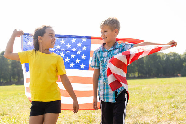 Дети сидят на открытом воздухе с американским флагом.