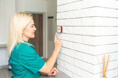 Kadın ısıyı evdeki beyaz duvara modern kablosuz termostatla düzenliyor. Akıllı ev ısıtma yönetmeliği kavramı