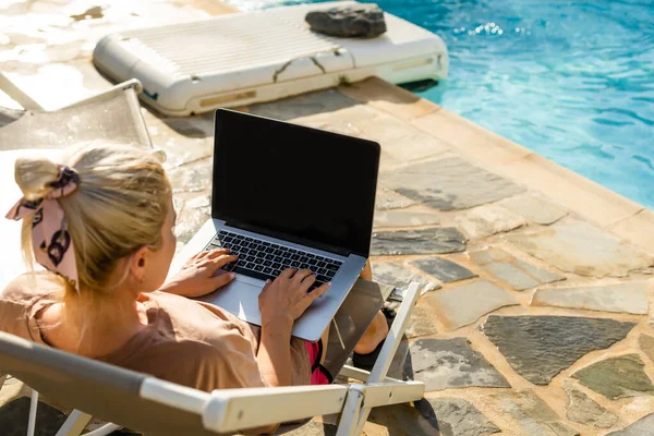 Trabalhamos mesmo em férias, jovem atraente encontra-se em uma espreguiçadeira perto da piscina com um laptop, mulher usa um laptop em férias para o trabalho, trabalho on-line — Fotografia de Stock