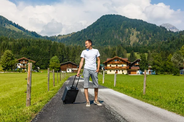 Reisender Mann, der mit Koffer auf der Straße in den Bergen unterwegs ist. Reisekonzept. — Stockfoto