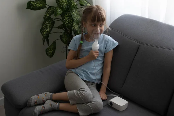 Nove anos de idade criança com asma alérgica, inalando sua medicação através do espaçador, enquanto olha com os olhos cansados — Fotografia de Stock