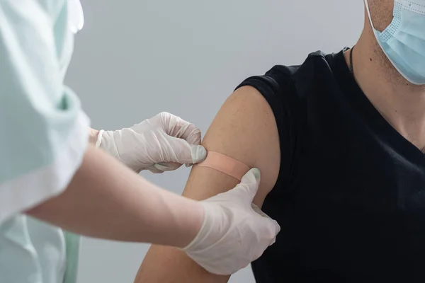 Läkaren vaccinerar en ung attraktiv man, får en injektion av Covid 19 coronavirus vaccin, tredje vaccinationen booster vaccination. — Stockfoto