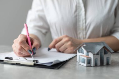 Rahat ofis masasının üzerinde ev modelini tutan genç bir kadının kesilmiş görüntüsü.