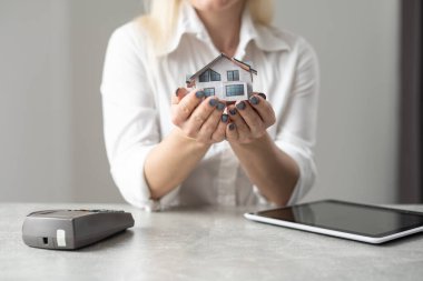 Rahat ofis masasının üzerinde ev modelini tutan genç bir kadının kesilmiş görüntüsü.