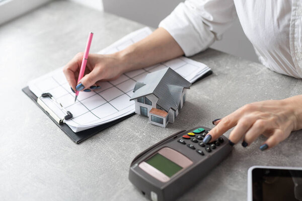 Cropped image of a young woman holding a house model over the comfortable office desk