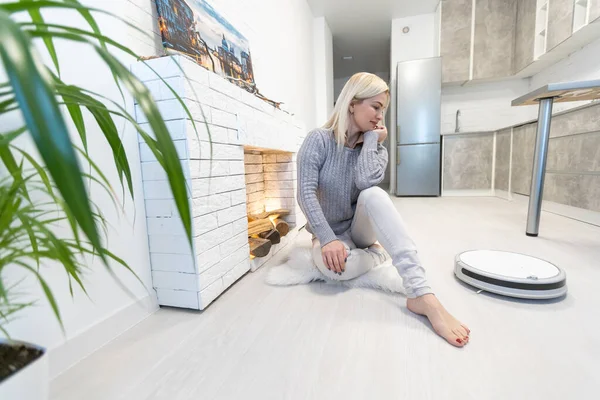Ung kvinna med hjälp av automatisk dammsugare för att rengöra golvet, styra smart maskin hushållsarbete robot — Stockfoto