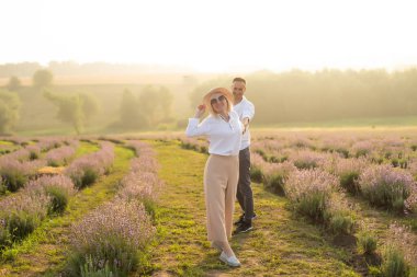 Gülümseyen genç çift lavanta tarlasında el ele tutuşuyorlar, yürüyorlar..