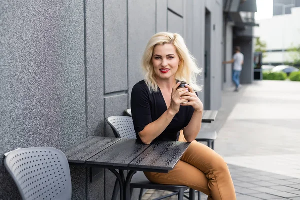 Stylová blondýnka sedí v kavárně na terase a pije kávu, užívá si víkend. — Stock fotografie