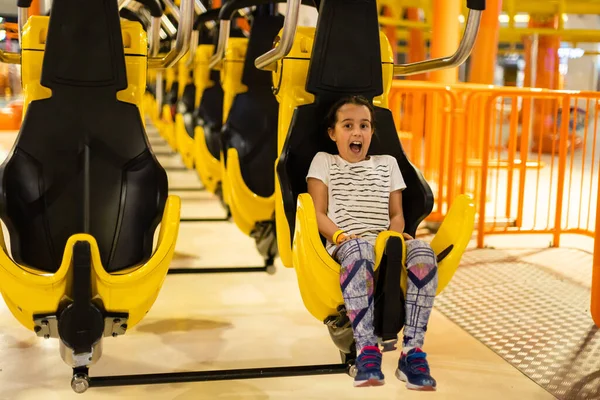 En liten flicka barn i ljusa kläder rider på en karusell i en nöjespark. — Stockfoto