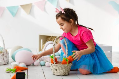 Paskalya 'ya hazırlanıyorum. Paskalya yumurtası tutan ve arka planda süslemelerle gülümseyen sevimli küçük kız.