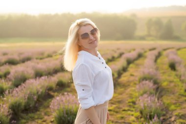 Lavanta tarlasında saman şapkalı genç sarışın gezgin lavanta çiçekleriyle çevrili.