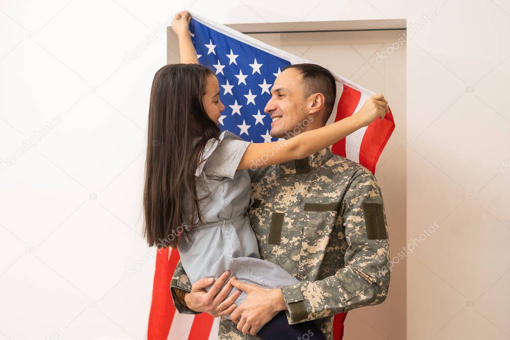 Happy little girl daughter with American flag hugging father in military uniform came back from US army, male soldier reunited with family at home.