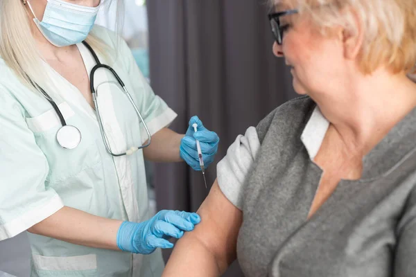 Концепция вакцинации. Пожилые люди получают иммунную вакцину под руку от прививок от гриппа, пневмонии и лишаев в больнице от медсестры. Врач делает инъекции пожилым пациентам в клинике — стоковое фото