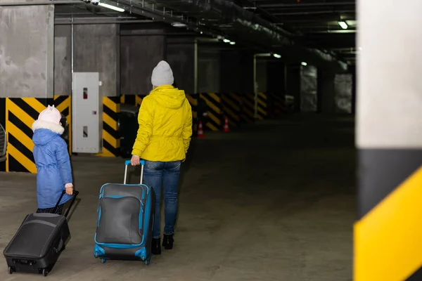 Yeraltı otoparkında tekerlekli bavul taşıyan anne ve kız. — Stok fotoğraf