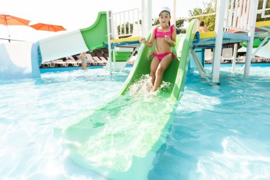 Yazın iki kız açık havuza su sıçratır. Mutlu çocuklar, kız kardeş oynuyor, halka açık havuzda güneşli havanın tadını çıkarıyor.