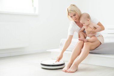 Toddler robot elektrik süpürgesinin yanında oturuyor. Yukarıdan bak. Ev işi. Alerji kontrolü