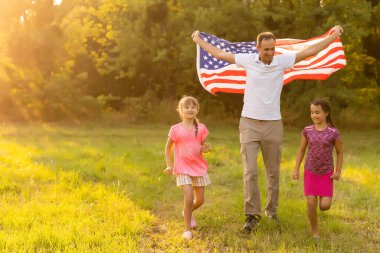 Gün batımında buğday tarlasında Amerikan bayrağı taşıyan mutlu bir aile. Bağımsızlık Günü, 4 Temmuz.