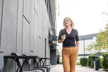 Güzel kadın ofis binası yürüyüş kahve ile çalışma olacak. İş için yolda elinde sıcak bir içecek fincan şehir sokak üzerinde tutan başarılı iş kadın portresi.