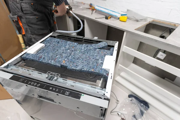 Técnico de electrodomésticos que trabaja bajo un fregadero de cocina instalando un lavavajillas — Foto de Stock