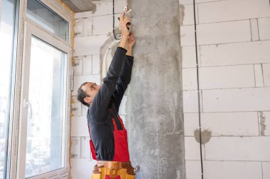 Yakışıklı genç elektrikçi ev inşaatı şantiyesinde çalışıyor.