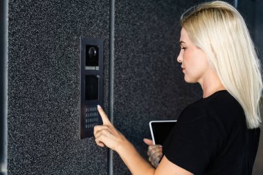 Kadın binaya girmek için dahili telefonu çeviriyor.