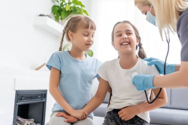 Küçük kız hastası olan genç bir doktor steteskopla tıbbi muayeneden geçiyor..