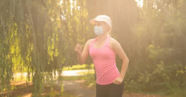 Bądź w formie podczas kwarantanny. Sportowa młoda kobieta biegnie na świeżym powietrzu, ma maskę ochronną na twarzy. Bieganie samemu z wirusem Corona lub Covid-19. — Zdjęcie stockowe