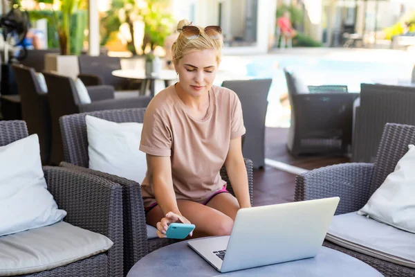 Νεαρή γυναίκα κάθεται σε φορητό υπολογιστή σε δημόσιο χώρο wifi, δακτυλογράφηση, οι άνθρωποι που περνούν από το παρασκήνιο — Φωτογραφία Αρχείου
