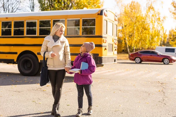 Mutter läuft mit Tochter zum Schulbus vor der Grundschule. — Stockfoto