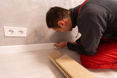 Etek tahtalarının kurulumu, ana yapıştırıcılar duvarın dış köşesine zemin silindirleri, eller.