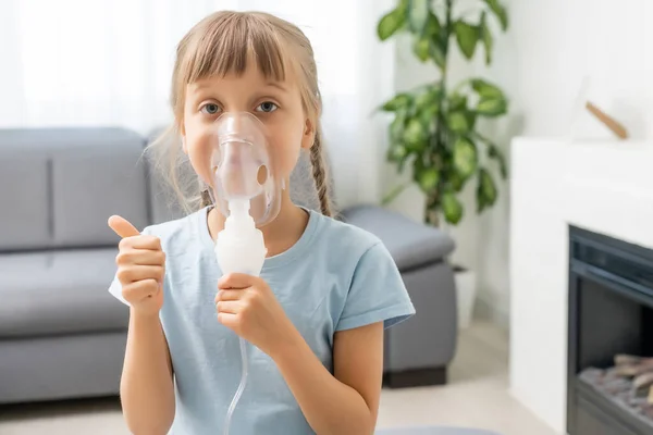 La niña hace inhalación con un nebulizador. niño enfermo sosteniendo el inhalador en la mano y respira a través de un inhalador en casa — Foto de Stock