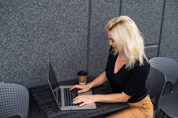 Jovem mulher usando smartwatch usando computador portátil. Feminino trabalhando em laptop em um café ao ar livre . — Fotografia de Stock