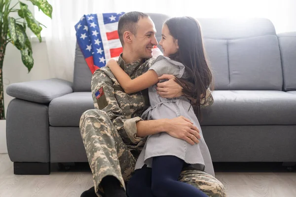 Retrato de feliz pai da família americana em uniforme militar e filha menina bonito com bandeira dos Estados Unidos abraçando e sorrindo para a câmera — Fotografia de Stock